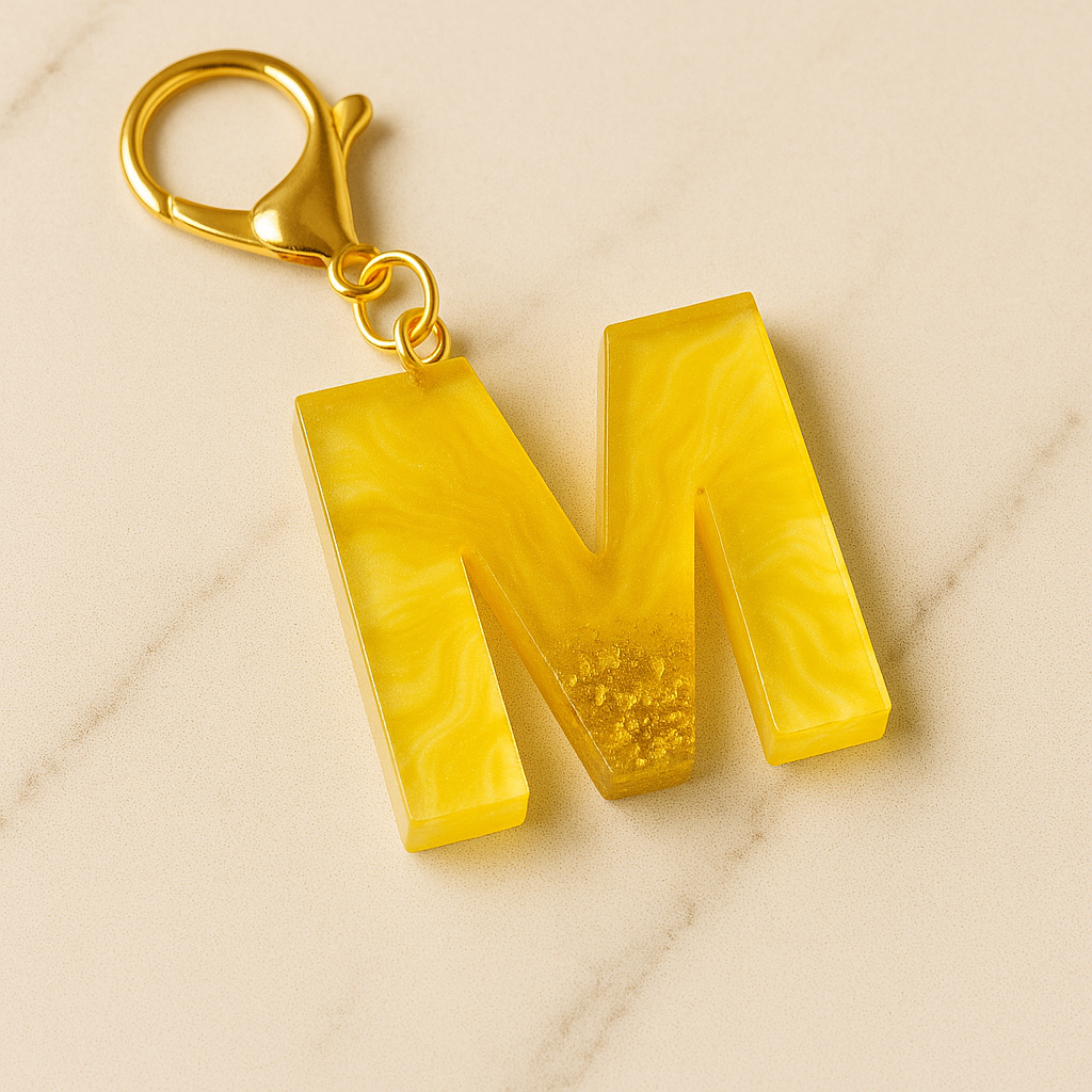 Yellow letter 'M' keychain on a beige marble background